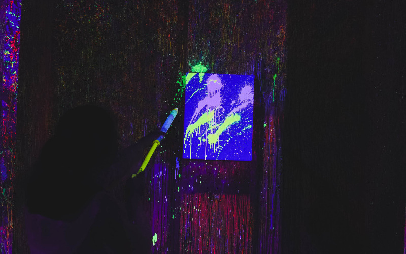 Glowing neon paint splashed on canvas under blacklight at Art Barn