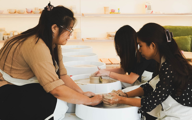 Tutor demonstrating pottery wheel throwing technique at Art Barn