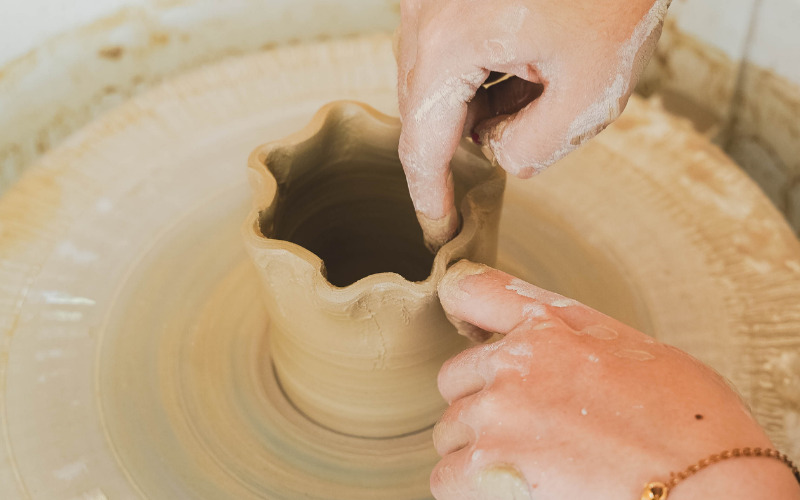 Hands shaping wet clay on a spinning pottery wheel during a wheel throwing class